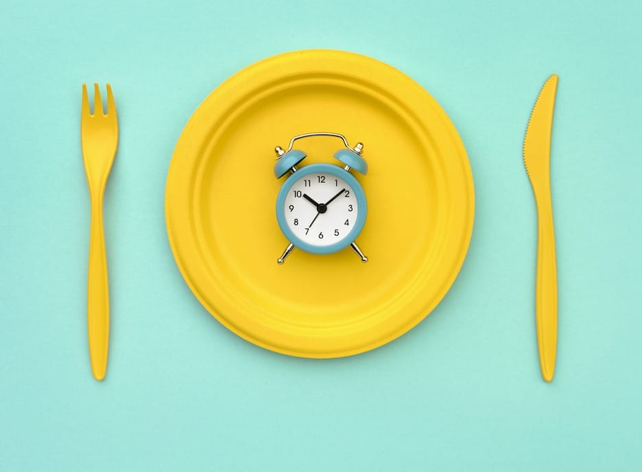 Intermittent fasting, lunch time, diet. Alarm clock, plate and cutlery. Yellow and blue colors.